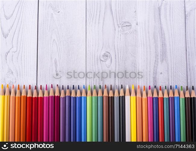 Colored wooden pencils viewed from above on a gray and white wooden background
