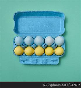Colored yellow blue Easter eggs in a blue cardboard box on a green background with copy space. Easter layout. Flat lay. A row of blue and a row of yellow Easter eggs in a carton on a green background with copy space. Easter composition.