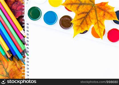 Colorful autumn leaves, multi-colored pencils and paint for painting near white paper with place for text. Background with autumn leaves. Copy space for inscription. School concept. Colorful autumn leaves, multi-colored pencils and paint for painting near white paper with place for text. Background with autumn leaves. Copy space for inscription.