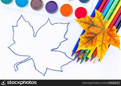 Colorful autumn leaves, multi-colored pencils and paint for painting near white paper with place for text. Background with autumn leaves. Copy space for inscription. School concept. Colorful autumn leaves, multi-colored pencils and paint for painting near white paper with place for text. Background with autumn leaves. Copy space for inscription.