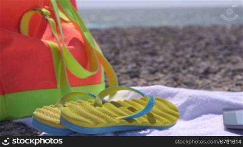 Colorful bag flipflops and towel at summer beach