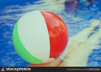 Colorful beach ball floating in pool. A woman&rsquo;s legs in the water.