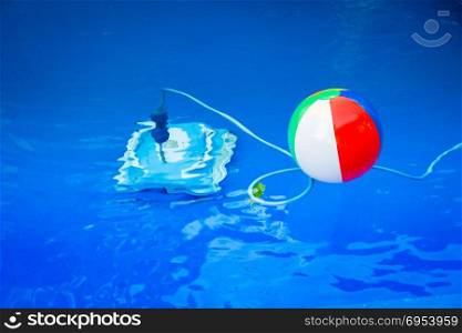 Colorful beach ball floating in pool and next to him underwater a cleaning robot.