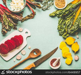 Colorful beetroot cooking preparation. Red and yellow sliced beetroot, chard leaves and ingredients on light blue kitchen table background, top view, frame. Vegan or vegetarian clean food concept
