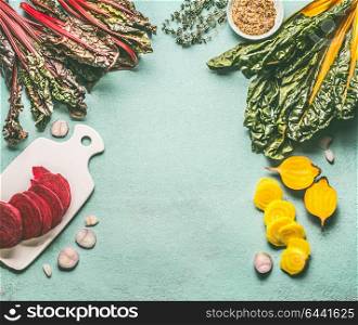 Colorful beetroot cooking preparation with red and yellow sliced beetroot, chard leaves and ingredients on light blue kitchen table background, top view, frame. Vegan or vegetarian clean food concept