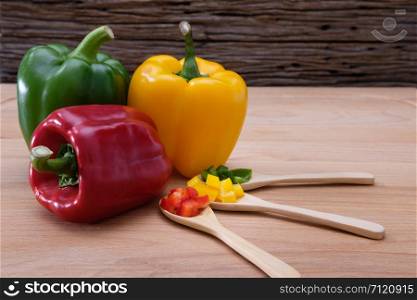 Colorful bell peppers and kitchen utensil on white wooden table.