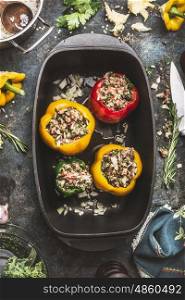 Colorful bell stuffed paprika peppers in iron cooking pot on dark rustic kitchen table background, top view