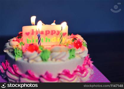 Colorful birthday cake with candles lights on the table at night with label of happy birthday