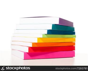 Colorful books are outlined in the colors of the rainbow. Stacked of the books on a shelf near the white wall. Colorful collection of the books on white