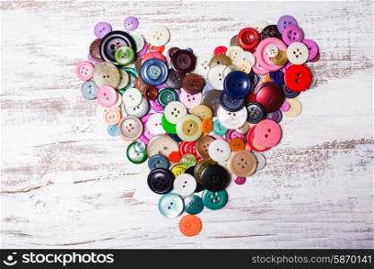 Colorful buttons as a heart shape on the vintage wooden table. Colorful buttons
