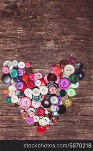 Colorful buttons as a heart shape on the vintage wooden table. Colorful buttons