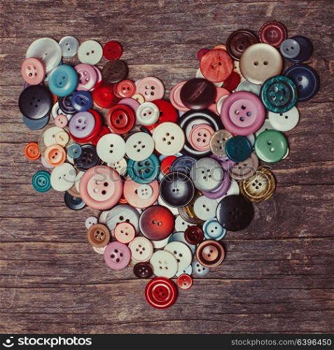 Colorful buttons as a heart shape on the vintage wooden table. Colorful buttons heart