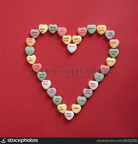 Colorful candy hearts with sayings on them arranged in shape of heart on red background.