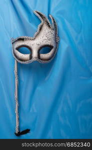 Colorful carnival mask on wavy blue satin fabric background.