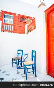 Colorful chairs and table on street of typical greek traditional village with white houses on Mykonos Island, Greece, Europe. Cute cafe on the street of typical greek traditional village on Mykonos Island, Greece, Europe