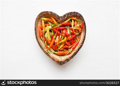Colorful chili peppers in wooden dish heart shape.. Colorful chili peppers in wooden dish heart shape on white.