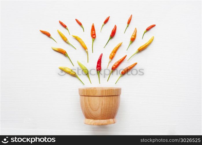 Colorful chili peppers with wooden mortar on white.