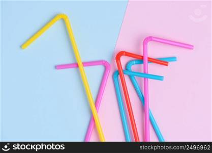 Colorful cocktail straws chaotically lay on blue and pink soft trendy pastel colored paper background with side copy space