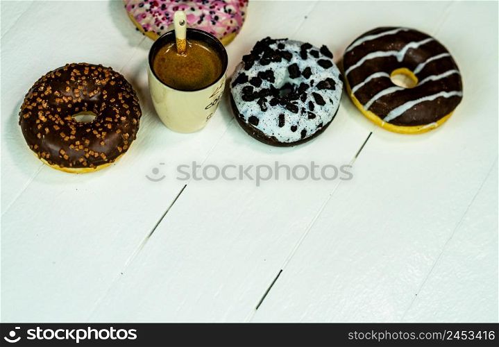 Colorful donuts and coffee cup on white wooden table. Sweet bakery with glazed sprinkles, breakfast concept. Top view with copy space