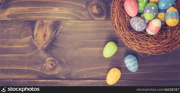 Colorful easter egg and nest on wooden background with space.