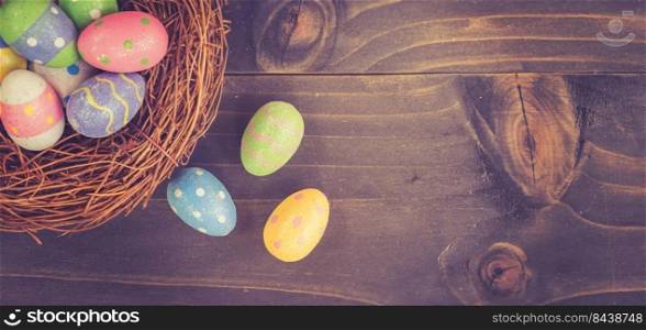 Colorful easter egg and nest on wooden background with space.