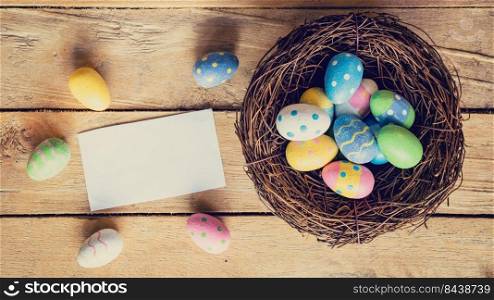 Colorful easter egg in nest and paper card on wood background with space.