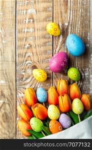 colorful easter eggs and bouquet of tulips on wooden background with space for a text, top view
