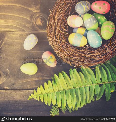Colorful easter eggs in neat and green leave on table wooden background with space.