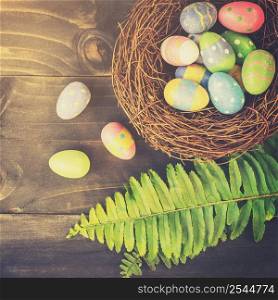 Colorful easter eggs in neat and green leave on table wooden background with space.