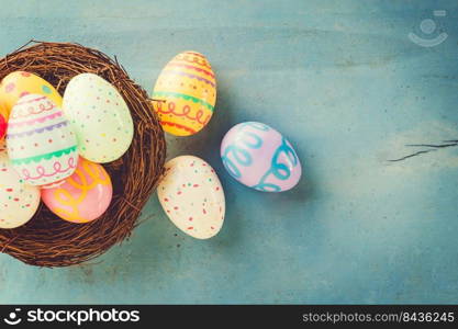 Colorful easter eggs in nest on blue wood background with copy space.