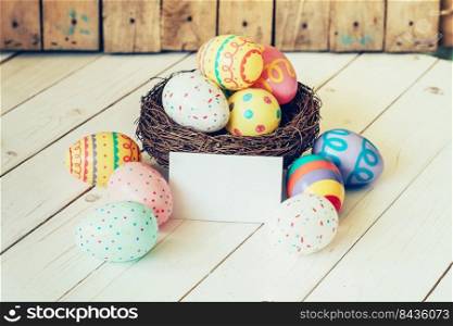 Colorful easter eggs in the nest and paper card on wood table background.