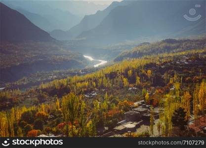 Colorful foliage in autumn season. Nature background of forest and river against Karakoram mountain range in Hunza Nagar Valley. Gilgit Baltistan, Pakistan.