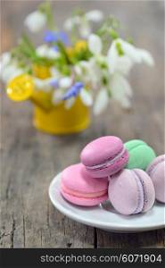 Colorful French Macarons and spring flowers on wooden background