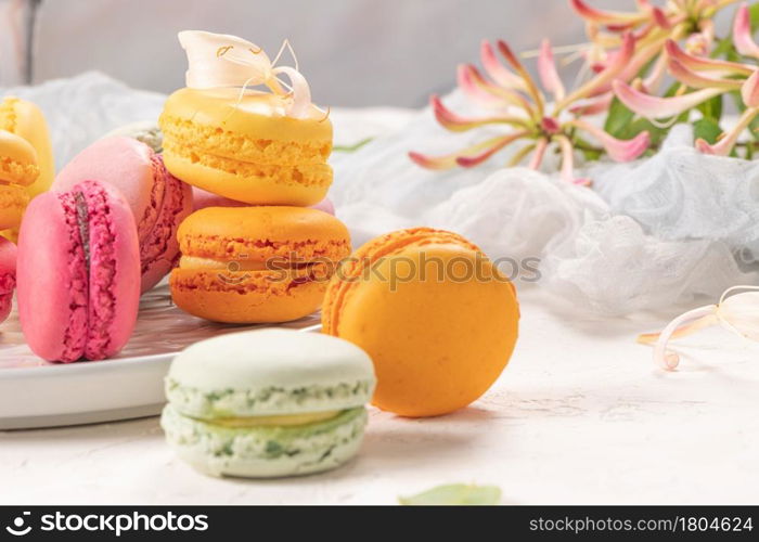 Colorful french macaroon cakes. Macaroons with jasmine flowers on white table background. Selective focus