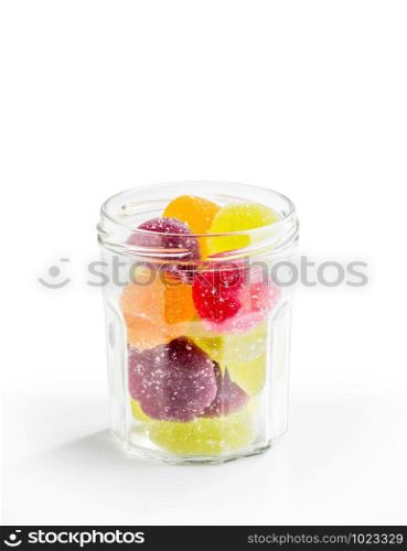 Colorful fruit jelly in open glass jar, on white background