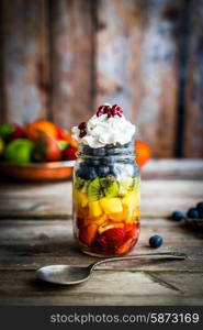 Colorful fruit salad in a jar on rustic wooden background