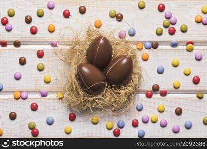colorful gem candies surrounded around chocolate easter eggs nest wooden table