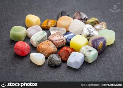 colorful gemstones on slate stone. a pile of polished, semiprecious, colorful gemstones against gray slate stone