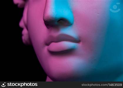 Colorful gypsum copy of ancient statue of human head for artists on a black background. Close up view lips. Plaster sculpture of human face. Toned blue and purple. Cyberpunk, surreal style poster.. Colorful gypsum copy of ancient statue of human head for artists on a black background. Close up view lips. Plaster sculpture of human face. Toned blue and purple. Webpunk, surreal style poster.