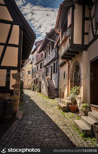 colorful halftimbered houses along a narrow street with cobblestones in the medieval town of Eguisheim, Alsace Region, France