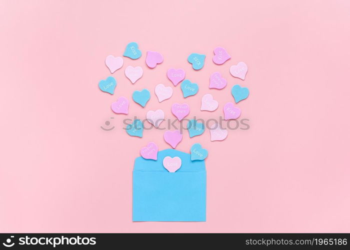 Colorful hearts with text LOVE, KISS, FOREVER YOURS fly out in the form of heart from blue paper envelope on pink background . Valentines day concept. Gift for lover. love confession Copy space.. Colorful hearts with text LOVE, KISS, FOREVER YOURS fly out in the form of heart from blue paper envelope on pink background . Valentines day concept. Gift for lover. love confession Copy space