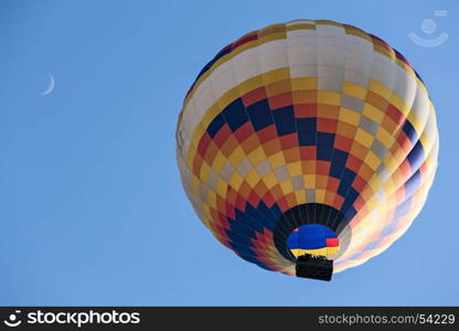 Colorful hot-air balloon in flight and moon seen from below against a blue sky. Colorful hot-air balloon in flight and moon seen from below