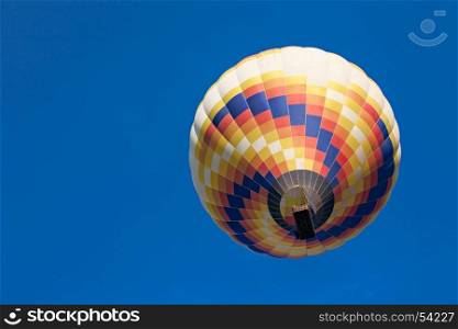 Colorful hot-air balloon in flight seen from below against a blue sky. Colorful hot-air balloon in flight seen from below