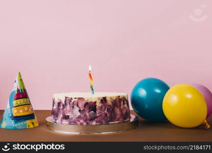 colorful illuminated candle birthday cake with party hat balloons desk against pink background