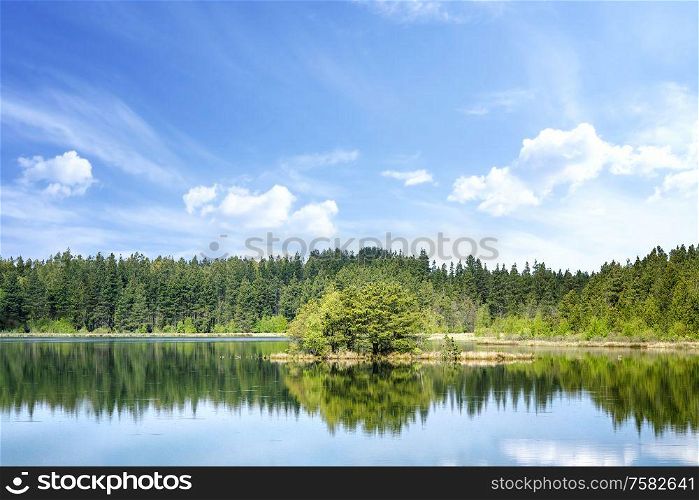 Colorful lake scenery with reflections of trees in the water and with a small island in the middle
