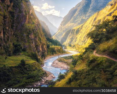 Colorful landscape with high Himalayan mountains, beautiful curving river, green forest, blue sky with clouds and yellow sunlight at sunset in summer in Nepal. Mountain valley. Travel in Himalayas. Summer landscape with mountains, river at sunset