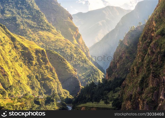 Colorful landscape with high Himalayan mountains, green forest, blue sky with clouds and yellow sunlight at sunrise in summer in Nepal. Mountain valley in the morning. Travel in Himalayas. Nature. Colorful landscape with mountains, river at sunrise in summer