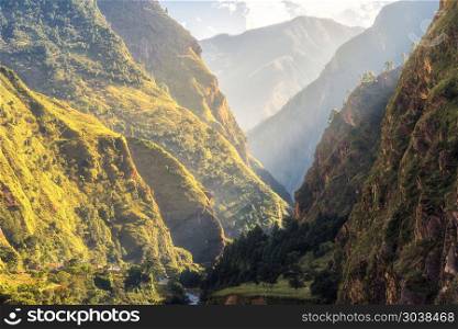 Colorful landscape with high Himalayan mountains, green forest, blue sky with clouds and yellow sunlight at sunrise in summer in Nepal. Mountain valley in the morning. Travel in Himalayas. Nature. Colorful landscape with mountains, river at sunrise in summer