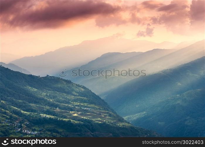 Colorful landscape with Himalayan mountains, beautiful hills with green meadows, forest, orange sky with clouds and yellow sunlight at sunset in summer in Nepal. Mountain valley. Travel in Himalayas
