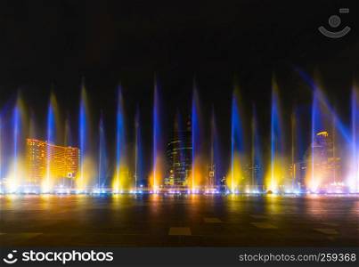 Colorful lights with blurry fountain, water show on black background in city at night